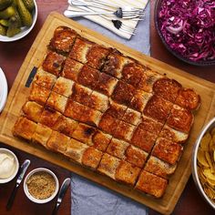 a wooden cutting board topped with sliced up food next to bowls of vegetables and pickles