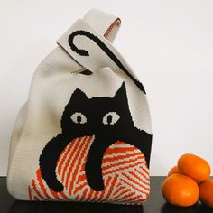 a white bag with a black cat on it next to oranges