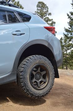 the rear end of a white suv parked on dirt