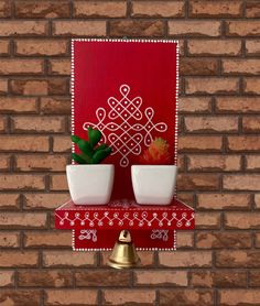 there is a red and white wall hanging with two cups on the shelf next to a potted plant