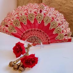 a red fan and two roses on a white table with gold trimmings next to it