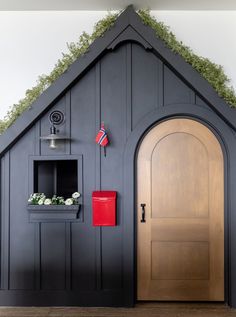 a black house with a wooden door and green grass growing on the roof is shown