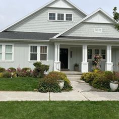 a gray house with white trim and lots of flowers in front of the entrance door