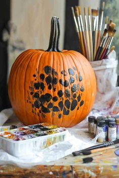 an orange pumpkin with black spots on it sitting next to paintbrushes and other art supplies