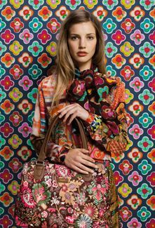 a woman holding a handbag in front of a wall with colorful flowers on it