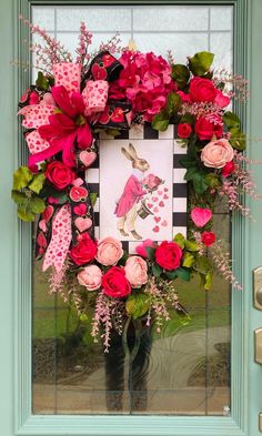 a pink and red wreath on the front door with roses, leaves and an image of a rabbit