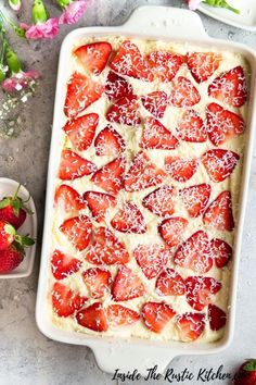 strawberry shortcakes in a white baking dish with strawberries on the side and pink flowers behind them