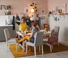 two people sitting at a table in a pink and white kitchen with sunflowers