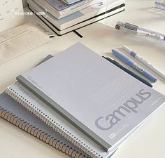 three notebooks are sitting on a table with pens and pencils next to them