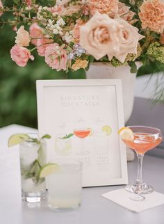 a table topped with two glasses filled with cocktails next to a sign that says signature cocktails