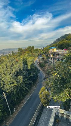 an empty road in the middle of some trees and buildings on top of a hill