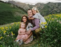 a man, woman and child are sitting on a hill with wildflowers in the foreground