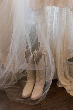 two pairs of white cowboy boots sitting on top of a wooden floor next to a window