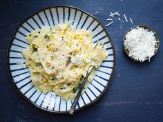 a white plate topped with pasta and parmesan cheese next to a bowl of grated parmesan