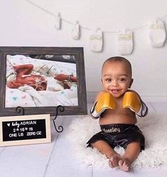 a baby with boxing gloves sitting in front of a photo frame on a white rug