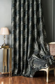 a living room with wood floors and a large window covered in black leaf print curtains