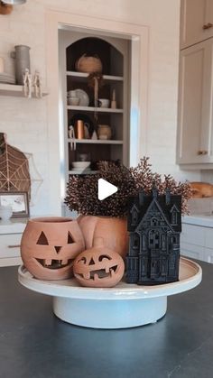 two pumpkins sitting on top of a cake plate with carved faces and houses in the background