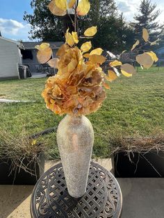 a vase filled with flowers sitting on top of a metal table in front of grass