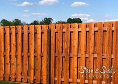 a wooden fence with the name stain & seal experts on it in front of some grass and trees