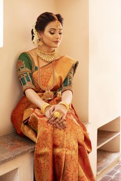 a woman in an orange and green sari sitting on a bench with her hands together