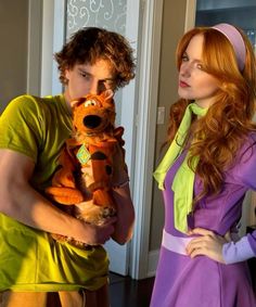 a man holding a stuffed animal next to a woman in a green and purple dress