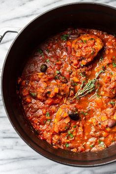 a pot filled with meat and vegetables on top of a marble countertop next to a spoon