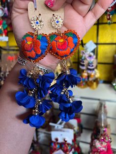 a person holding up some colorful earrings in their hand with other items on the table behind them