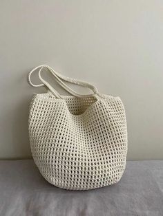 a crocheted white purse sitting on top of a bed next to a wall