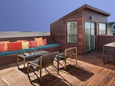 a wooden deck with chairs and tables on it, next to a small shed house