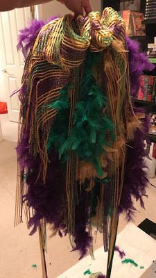 a person is holding up a purple and green feathered hat on top of a table