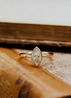 a pear shaped diamond ring sitting on top of a wooden table next to a book