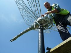 a man standing next to a large metal object on top of a wooden platform in front of a blue sky