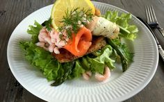 a white plate topped with lettuce, shrimp and lemon wedges on top of a wooden table