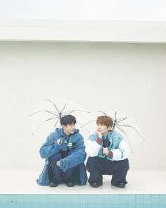 two boys sitting under umbrellas in front of a swimming pool