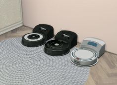 three robotic vacuums sitting on top of a rug in the corner of a room