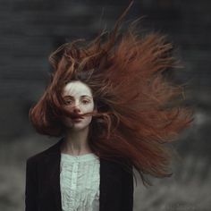 a woman with long red hair flying through the air in front of her face and body