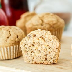 three muffins sitting on top of a wooden cutting board next to an apple