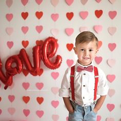 a young boy wearing suspenders and bow tie standing in front of a backdrop with hearts