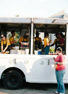 a woman standing in front of a food truck with people getting food from the back