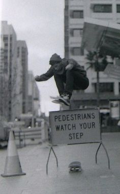 a man on a skateboard jumping over a sign that says pedestrians watch your step