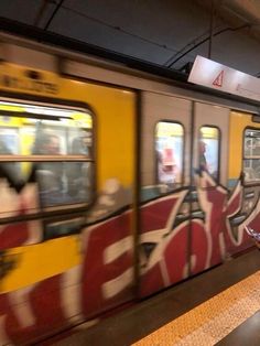 a subway train with graffiti on it's side is passing by people in the station