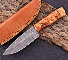 a knife sitting on top of a piece of wood next to a leather sheathed blade