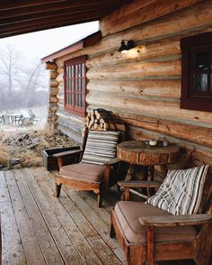 an old log cabin with two chairs and a table on the front porch in winter