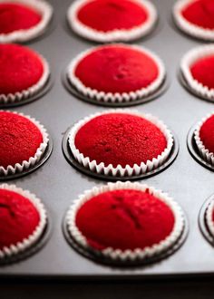 red cupcakes with white frosting sitting in a muffin tin, ready to be baked