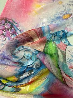 a multicolored scarf is laying on a white surface with flowers and butterflies painted on it