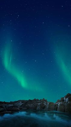 two green aurora bores are in the sky above some rocks and water at night