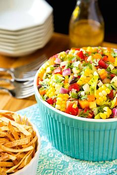 a colorful salad in a blue dish next to some chips