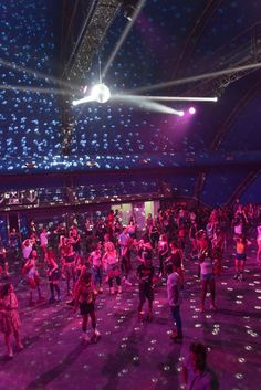 a group of people dancing in a large room with blue lights on the ceiling and floor