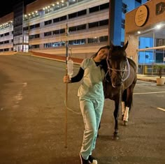 a woman standing next to a brown horse on a parking lot at night with a pole in front of her