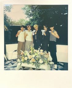 a group of young people standing next to each other in front of a table with flowers on it